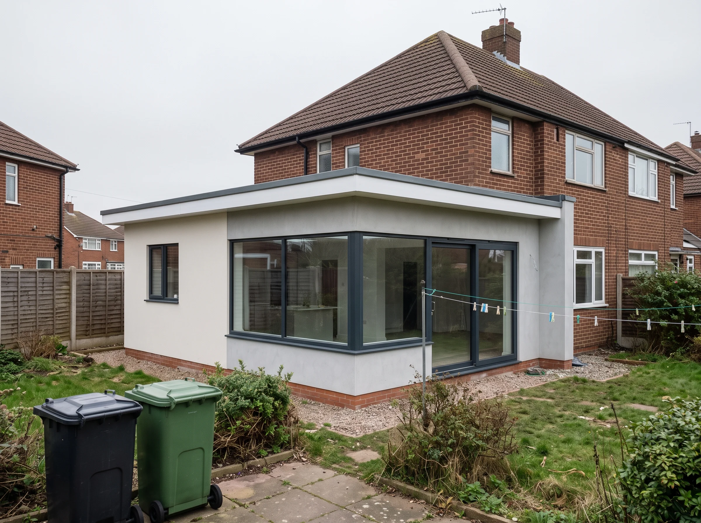 A wrap-around extension with corner glazing and sliding doors on the back of a brick semi-detached house, with a lawn and wheelbins in the foreground.
